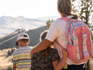 A woman with her arm around a girl look toward the mountains, backs to camera