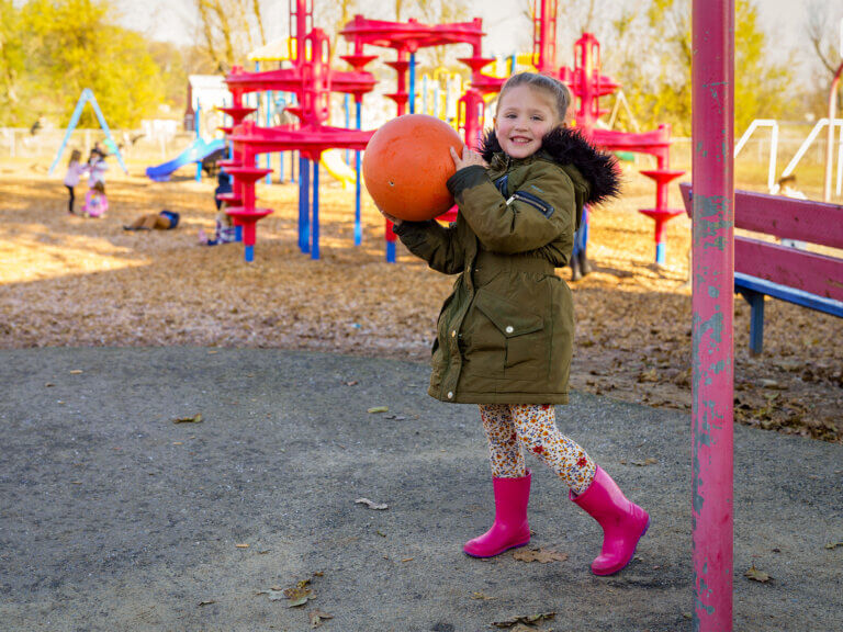 A young girl plays with a ball on a school playground.