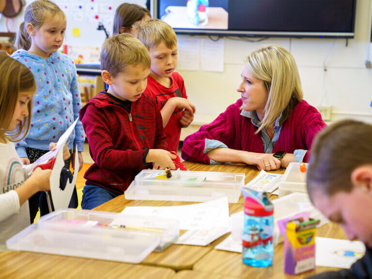 A teacher works with a group of young students on a project at a table.