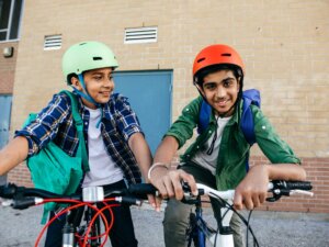 Two boys wearing helmets recline on their bikes.